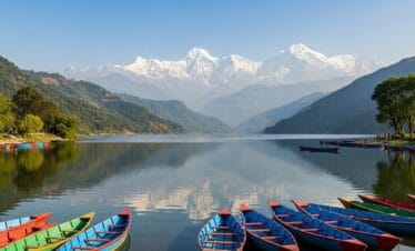 Phewa Lake in Pokhara Nepal with calm reflective waters, colorful boats, and Annapurna mountains in background, highlight of Pokhara Nepal trip
