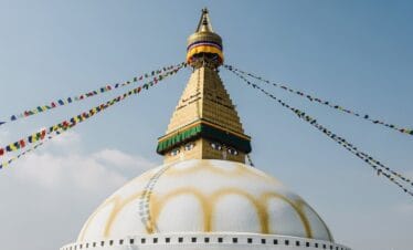 Close-up view of Boudhanath Stupa Kathmandu with white dome and fluttering prayer flags against blue sky